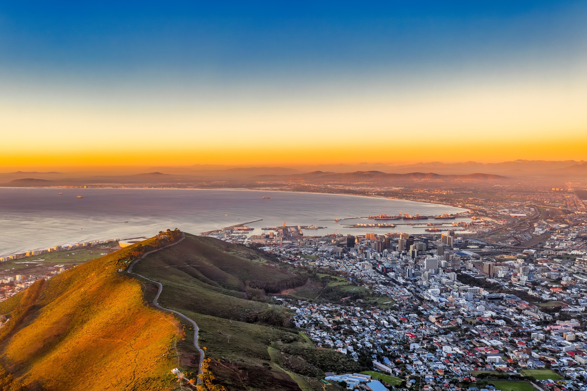 Panorama aérien du Cap depuis la montagne de la Table au coucher du soleil, soleil brillant sur la chaîne de montagnes, peu de navires dans le port déchargement, industriel, ville au crépuscule